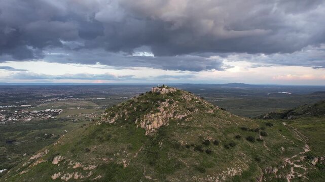 Cinematic drone footage approaching the summit of Cerro del Picacho in Aguascalientes, Mexico. Dramatic storm clouds gather above the mountain while expansive landscapes stretch across the horizon.