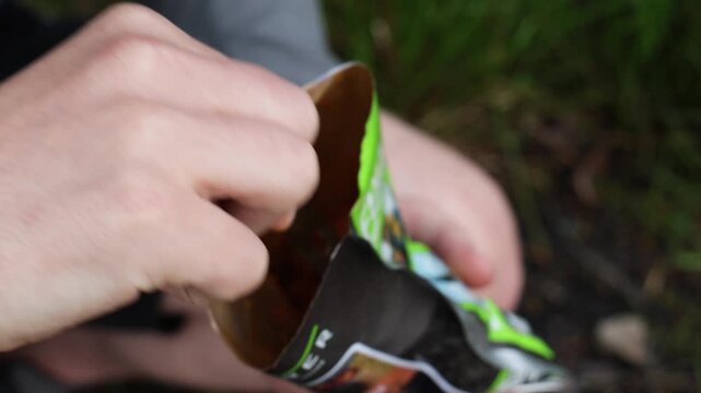 Camping meal pouch close-up as a person scoops dehydrated trail food with a fork from a foil package outdoors, showing backcountry cooking and adventure travel dining.