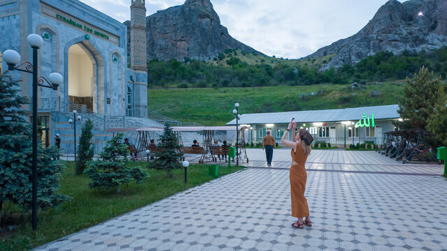 Kyrgyzstan, Osh - May 8, 2026: A girl stands in awe near the stunning Sulaiman-Too mosque, surrounded by lush mountains in Osh, Kyrgyzstan. The serene atmosphere invites visitors to explore.