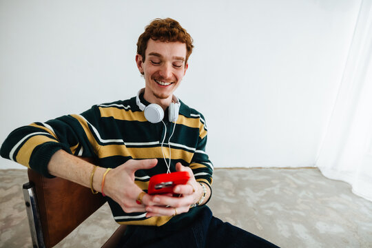 Gen Z man using smartphone with headphones for mobile entertainment indoors