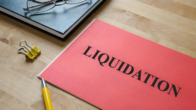 A red folder with liquidation text on a wooden desk with office supplies
