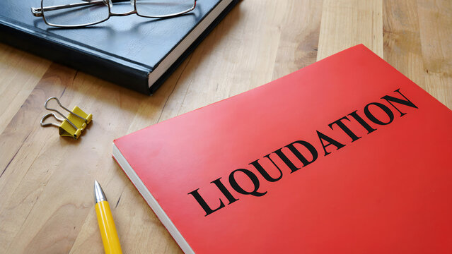 A red folder labeled liquidation with office supplies on a wooden desk
