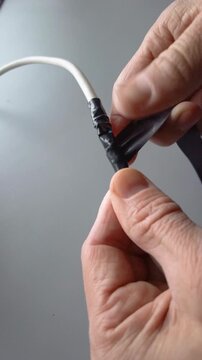 Securing and inspecting cable splice. Hands finishing and checking cable joint seal. Closeup of white hands completing secure and polished cable splice with careful inspection