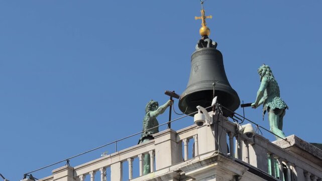 Bronze statues flank silent bell above urban tower