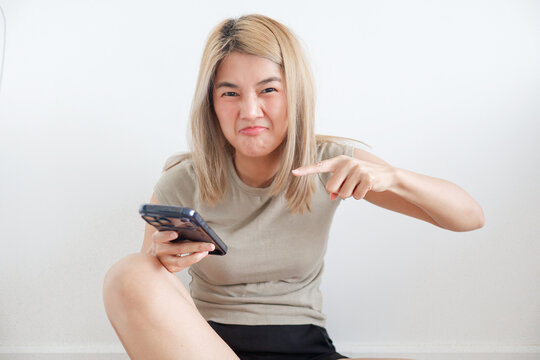 Annoyed Asian girl pointing accusingly at her mobile phone screen with a grumpy face.