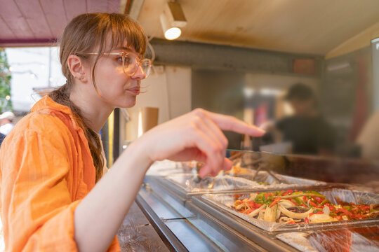 Woman orders food from a food stall in an outdoor market during a sunny day in a city