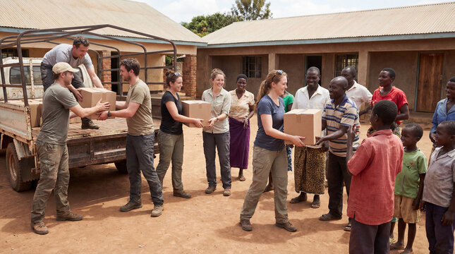 Volunteers hand cardboard boxes from truck to smiling local families near village homes showing humanitarian aid teamwork community support relief delivery  global development nonprofit effort