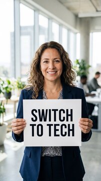 Smiling middle-aged latina businesswoman holding a switch to tech sign in a modern office