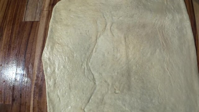 Top-down view close up of baker hands shaping fresh dough on a wooden work surface, preparing to make traditional Venezuelan Christmas dish of Pan de Jam&oacute;n