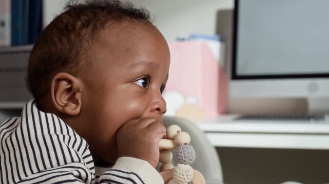 Closeup portrait of African American infant looking at camera and chewing wooden teething toy in pediatrician office. Footage is ideal for pediatric healthcare and baby wellness marketing campaigns