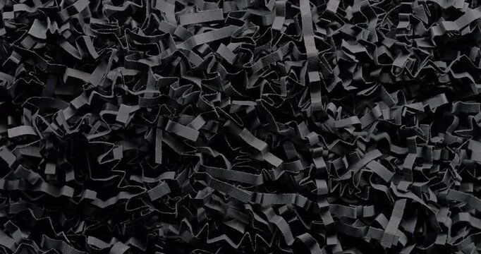 Black shredded paper. Close-up of dense black cut and crumpled paper strips forming chaotic layered texture. Smooth continuous rotation reveals dynamic shifts in light and deep shadows.