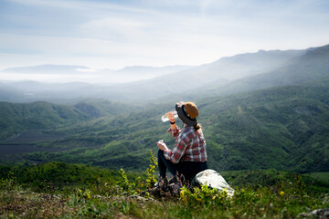 Fototapeta premium Woman taking a break during a mountain trek and drinking water surrounded by scenic nature. Wellness, recreation and adventure travel.