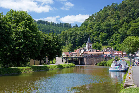 Lutzelbourg mit der St.-Michael-Kirche und dem Rhein-Marne-Kanal, auf dem ein Hausboot zu sehen ist