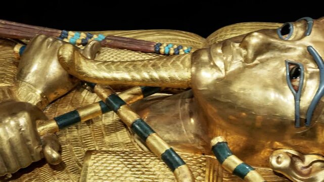 Extreme closeup of Tutankhamun solid gold inner coffin with crook scepter and blue inlay details on black background. Priceless royal Egyptian treasure.