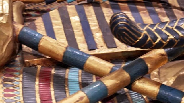 Extreme closeup of Tutankhamun solid gold inner coffin with crook scepter and blue inlay details on black background. Priceless royal Egyptian treasure.