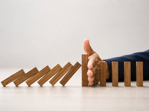 A human hand stopping a chain of falling dominoes, symbolizing crisis intervention and control.