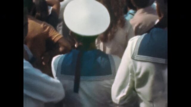 Unrecognizable sailors in naval uniforms stand among spectators during military parade near waterfront. Maritime tradition in naval culture. Old film. Archival retro 1960s. Vintage archive