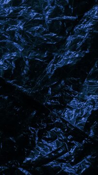 Close-up of shiny dark crinkled surface with sharp folds and reflective highlights. Smooth continuous rotation reveals dynamic shifts in deep shadows and bright specular reflections.