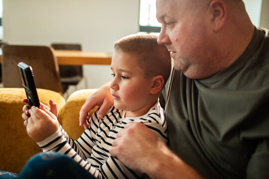 Father and son using smartphone on living room couch