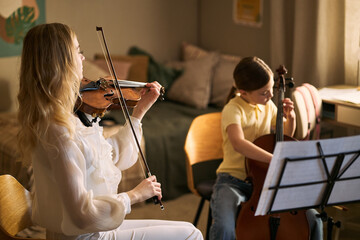 Caucasian woman teaching girl playing violin and cello while studying sheet music at home, supporting music education and creative skill development. Ideal for lesson ads or school promotion © DragonImages