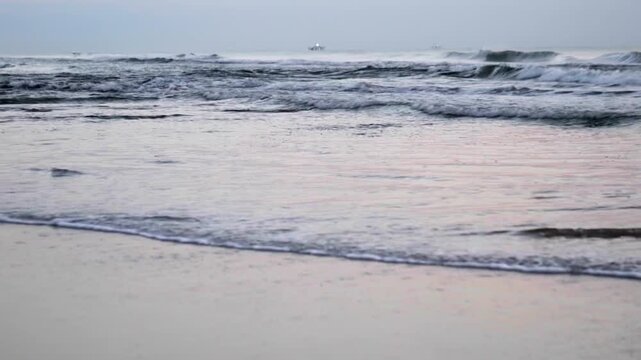 Beach waves in the early morning with shrimp boat anchored in background