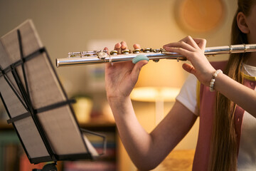 Child girl playing flute while reading sheet music during music lesson, practicing instrumental skills and arts education. Useful for school programs, tutoring, youth learning © DragonImages