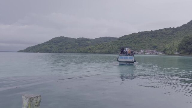 A traditional passenger boat operated by BUMO (Badan Usaha Milik Ohoi), Ngafan village's community-owned enterprise, departs from a stone pier and sails toward the open sea in Southeast Maluku