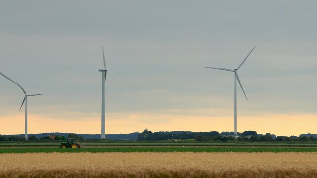 a tractor driving through the yellow field with wind turbine in the background, dutch agriculture