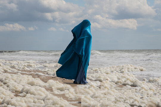 anonymous woman on the beach in blue dress and fabric standing in  foam of ocean
