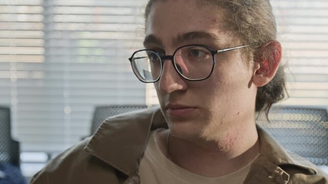Caucasian teenager with glasses looking down thoughtfully and listening during group therapy session. Footage for mental health awareness campaigns or youth counseling services