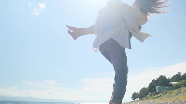 Two happy young people dressed in white shirts having fun on seashore. Handsome teenage boy happily spinning teenage girl while holding her in arms and laughing sincerely. Emotional family connection