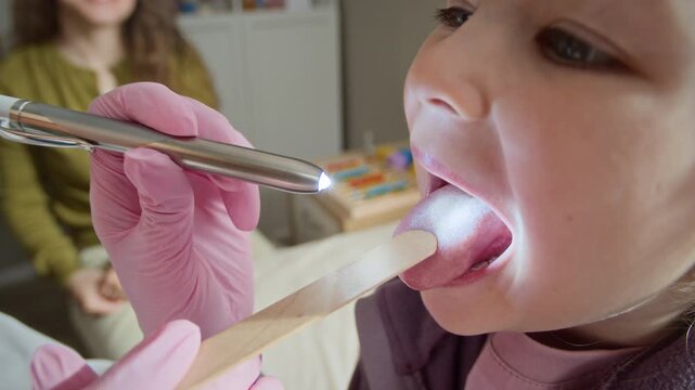 Closeup of Caucasian female pediatrician examining Caucasian childs throat using wooden tongue depressor and penlight during medical checkup. Footage is ideal for healthcare marketing and clinic ads