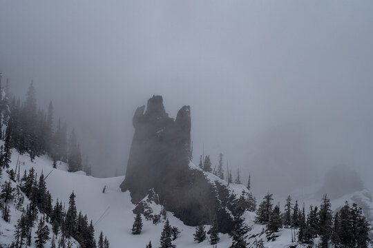 Aerial view of a jagged rock pinnacle on a snowy mountain slope surrounded by pine trees and thick fog along the Million Dollar Highway in Ouray, Colorado, United States.