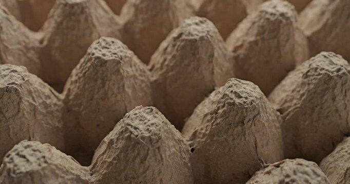 Recycled paper. Close-up of empty beige molded pulp tray with rough fibrous surface and conical cells. Smooth continuous rotation shows subtle light and shadow shifts across the eco recycled texture.