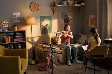 School age girls studying music and playing flute during home lesson, practicing reading sheet music and instrument skills. Useful for music education, tutoring, childhood learning © DragonImages