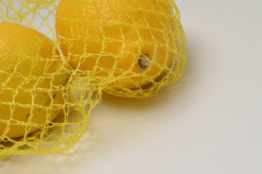 yellow lemon in a yellow mesh  on a white background corner composition hoirzontal layout, lemons close up with generous copy space,