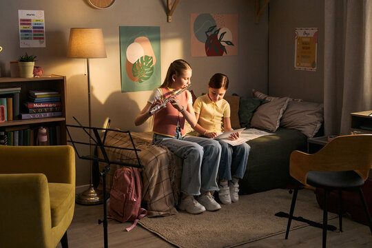 Wide shot of school age girls studying music, playing flute and reading sheet notes at home, practicing instrumental learning and creative education. For music school promotion or tutoring ads