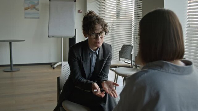Caucasian female psychotherapist wearing glasses talking and gesturing during counseling session with young Caucasian woman. Clip for mental health clinic promo