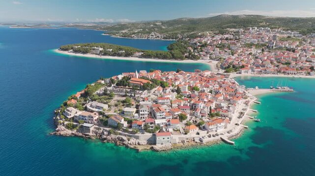 Drone circling in a half‑arc around Primo&scaron;ten&rsquo;s old‑town peninsula from the seaside, keeping the church tower and coastline in view over the bright Adriatic.