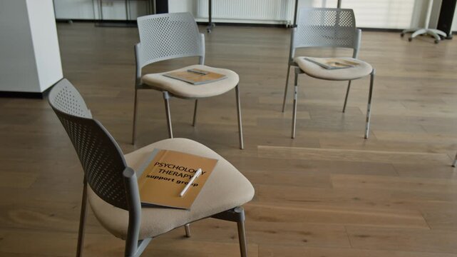 Empty chairs arranged in circle for group therapy session with psychology support group folder on foreground seat. Footage for mental health campaigns and counseling services