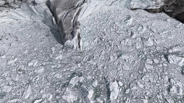 Aerial view of Fellaria glacier in the Italian Alps on a grey autumn day with a pan up from the icebergs in the frozen glacial lake up towards the alpine peaks surrounding the ice