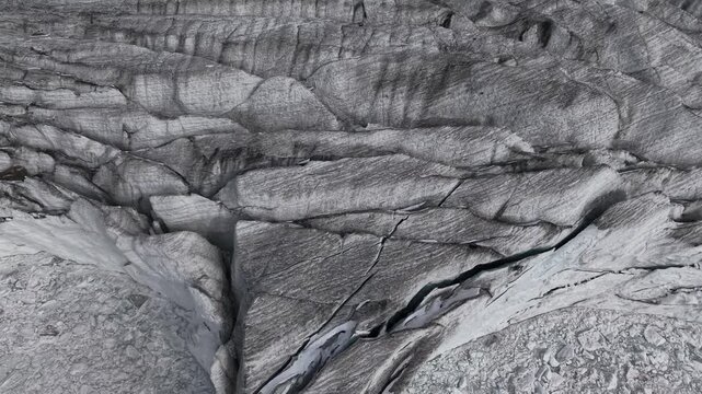 Aerial flyover over crevasses at the glacier tongue of Fellaria glacier in the Italian Alps bordering the frozen iceberg filled glacial lake with a top down view