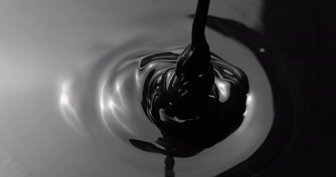 Black viscous liquid fast spiral. Close-up of thick black fluid flowing in rapid swirling spirals with white highlights. 