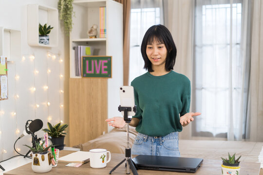 Young woman livestreams from home studio workspace, engaging with her online audience through a smartphone setup
