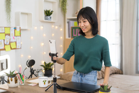 Cheerful woman reads comments and chats on her smartphone while live-streaming from home studio