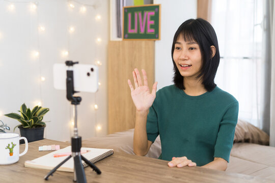 Cheerful young woman Greeting Viewers During Through Smartphone Video Streaming, creating engaging online content from Home Studio
