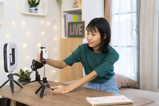 Cheerful Young woman prepares adjusting smartphone on table for a live broadcast in home studio