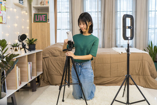 Young Content woman Setting Up Smartphone and Ring Light for Live Streaming, Vlogger Creating Social Media Content in Bedroom Studio