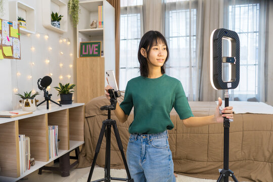 Young Content woman Setting Up Smartphone and Ring Light for Live Streaming, Vlogger Creating Social Media Content in Bedroom Studio