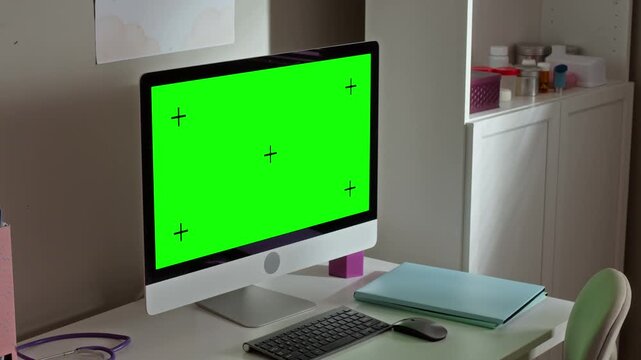 Computer monitor with green screen standing on desk in doctor office, stethoscope lying nearby. Mockup template ideal for healthcare software or medical website presentation